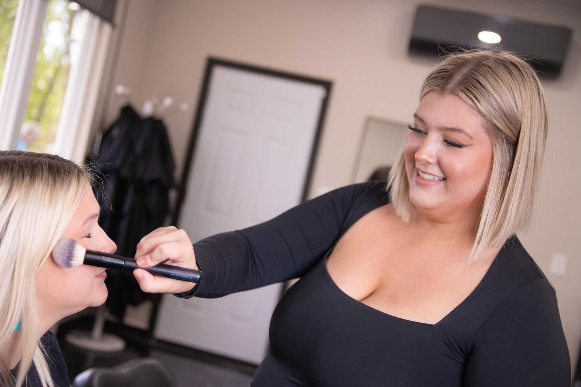 Makeup artist applying blush to a client's face in a salon setting.