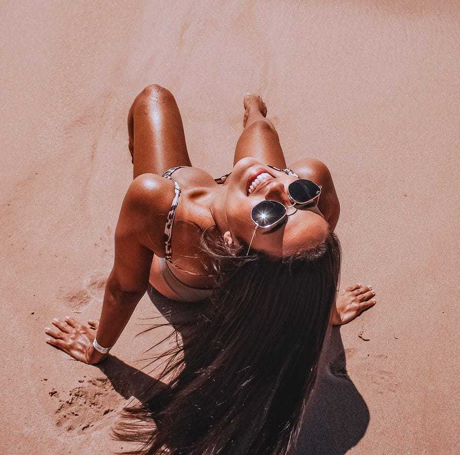 Woman in sunglasses smiling on a sunny beach.