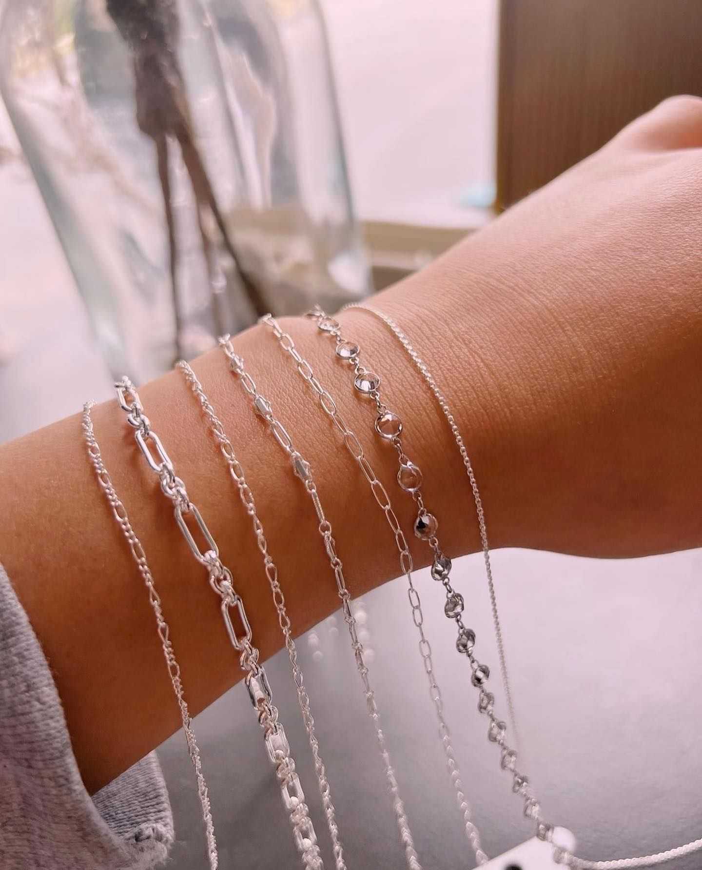A person's wrist adorned with various silver chain bracelets.