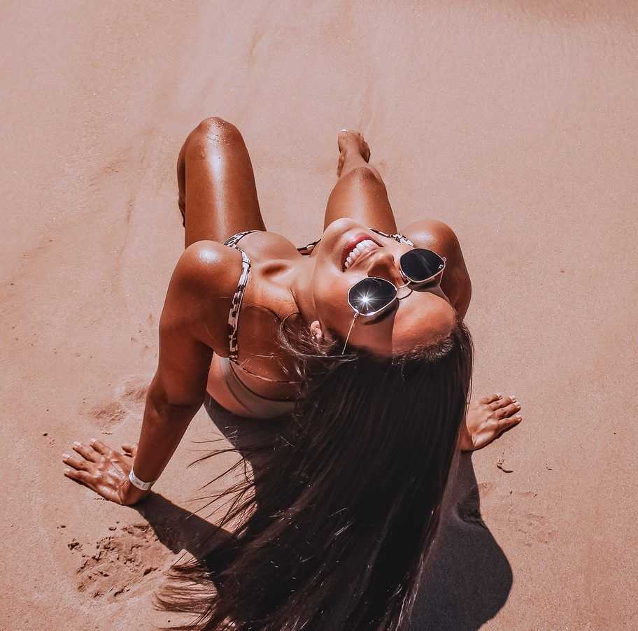 Woman in sunglasses smiling on a sunny beach.