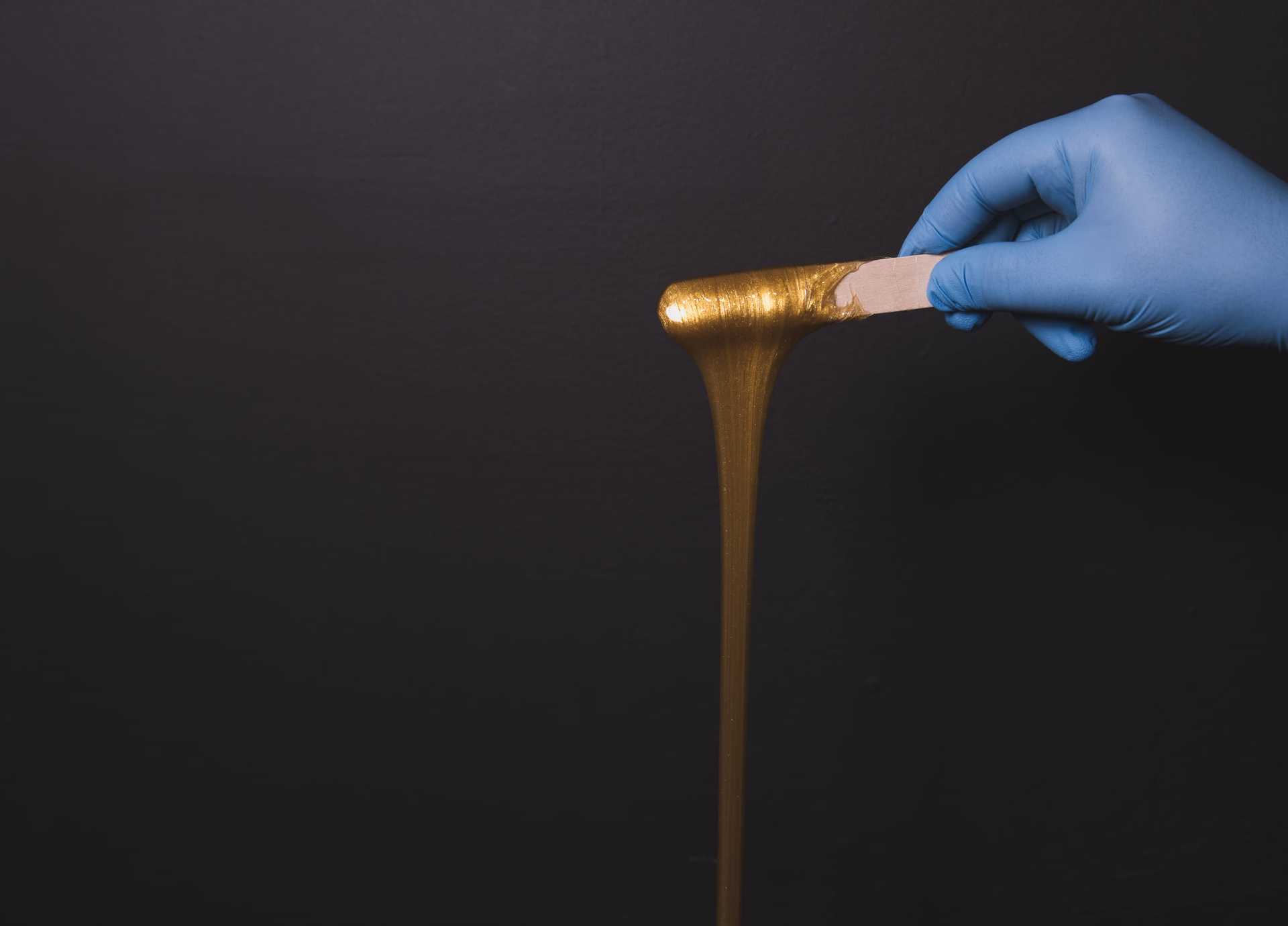 A gloved hand stretching shiny, golden slime against a dark background.