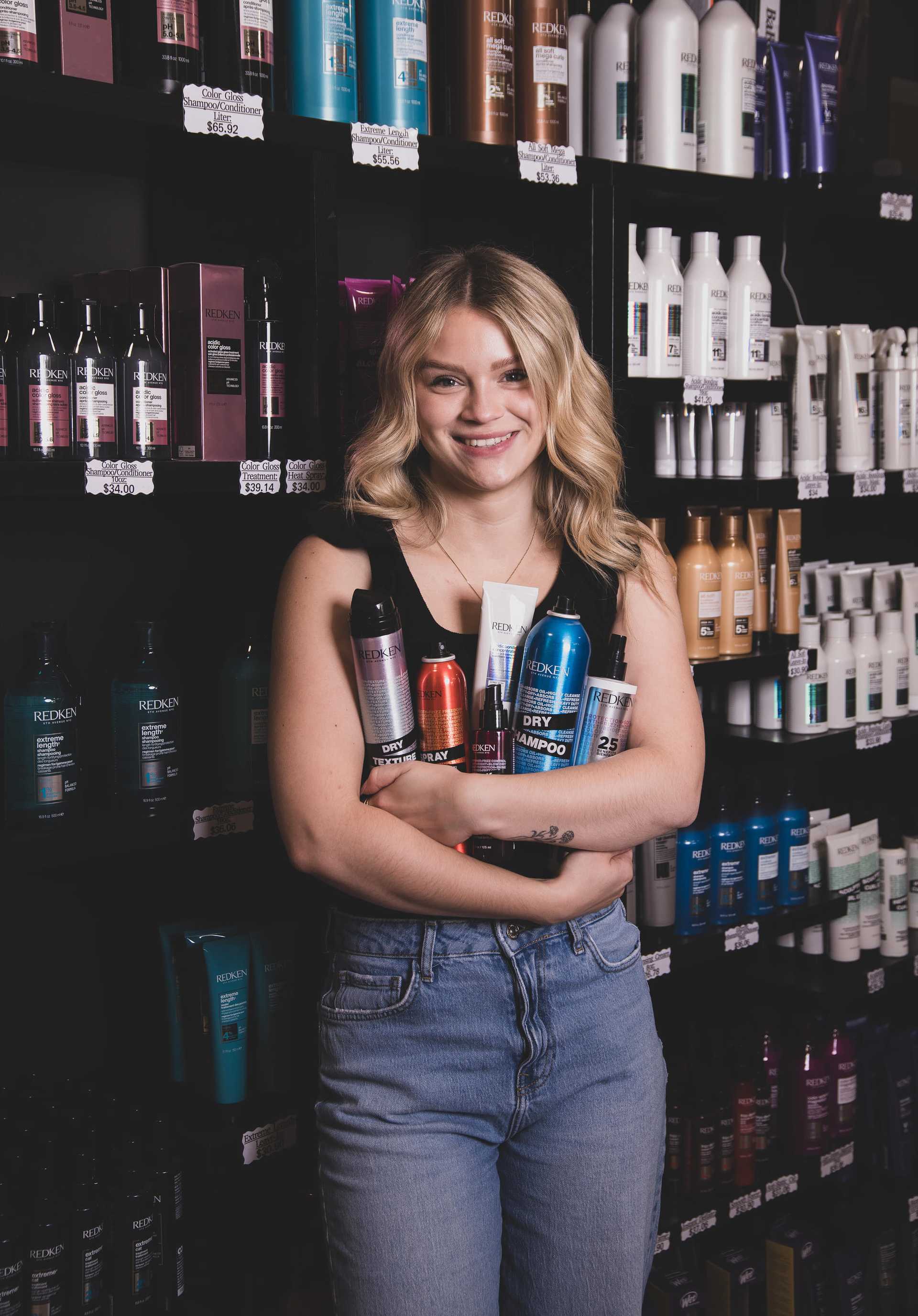 Smiling woman holding various hair care products in a store aisle filled with bottles.